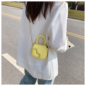 Fashionable yellow mini crossbody bag with gold chain strap in an outdoor street setting