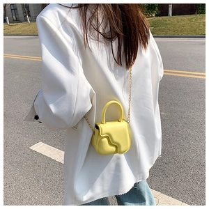 Detail of yellow mini crossbody bag with wavy texture and gold chain strap on model