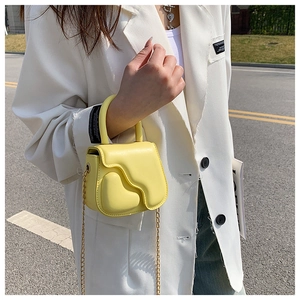 Detail of yellow mini heart bag with wavy flap and metal chain strap in street style