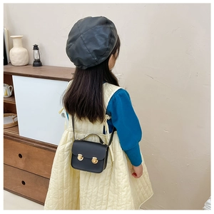 Détail d'un enfant portant un mini sac à main noir en similicuir avec boucles dorées
