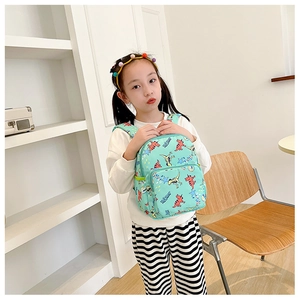Toddler modeling a light green canvas backpack featuring cute cartoon dinosaur prints