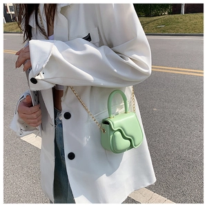 Detail of mint green mini bag with wave flap and gold chain strap on model
