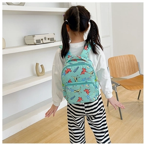 Rear view of a child wearing a green canvas backpack with colorful cartoon dinosaur prints