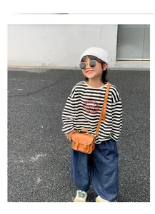 Détail d'un petit sac vintage marron pour enfant porté avec un t-shirt rayé