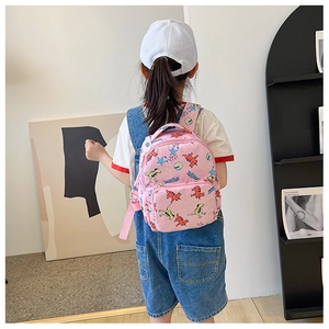 Pink canvas backpack with cartoon dinosaur print shown on a child in a home setting