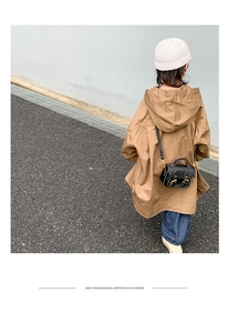 Détail d'un enfant portant un trench-coat à capuche marron avec un mini sac à bandoulière noir
