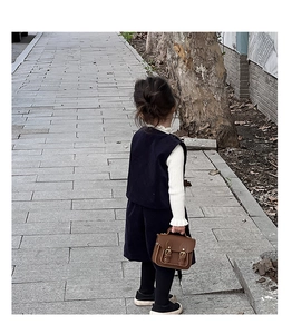 Détail d'un petit sac vintage en cuir marron avec une tenue pour enfants bleu marine