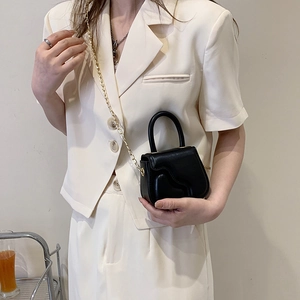 Minimalist black leather mini handbag with wavy texture and gold chain strap shown on model