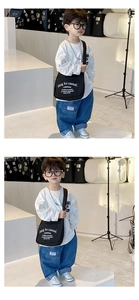 Detail of trendy kids' black canvas crossbody bag paired with loose denim jeans and white tee