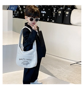 Outdoor shot of white canvas kids crossbody bag with black artistic lettering detail