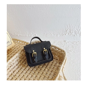 Détail d'un mini sac besace noir avec boucles dorées placé dans un panier tressé