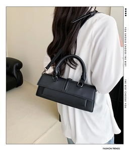 Close-up of black matte leather baguette bag showing shoulder strap and silver metal buckle