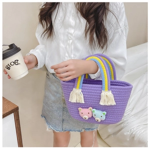 Détail d'un mini sac tissé violet avec des anses arc-en-ciel et des breloques d'ours