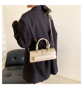 Detail view of a metallic champagne gold handbag with twin handles on a black blazer
