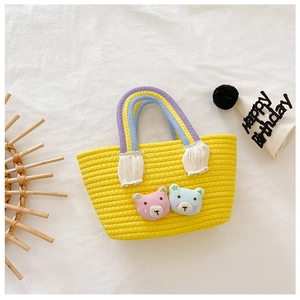 Détail d'un sac tressé jaune avec poignées arc-en-ciel et patchs d'ours mignons