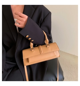 Detailed side view of caramel leather baguette bag held by model in black blazer