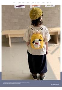 Close-up of yellow canvas kids backpack featuring a cute white plush puppy ornament