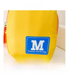 Detailaufnahme der gelben Kinder-Brusttasche mit blauem M-Buchstaben und orangefarbenem Zipper
