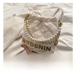 Detail of a quilted cream girls' bucket bag with pearl handle and golden logo charm