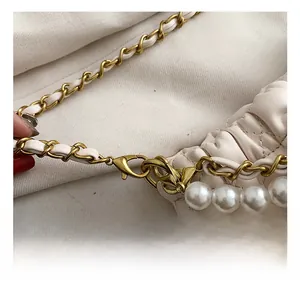 Detailed macro view of golden lobster clasp and pearl strap on white quilted handbag