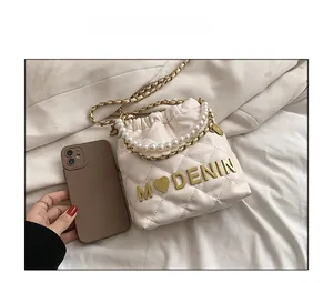 Detailed shot showing size comparison of cream quilted bucket bag with pearl handle