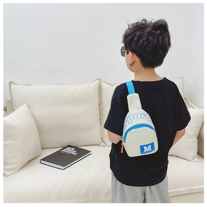 Mini-Brusttasche für Kleinkinder mit M-Print getragen von Kind auf weißem Sofa