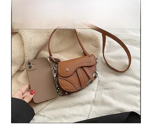 Gros plan d'un sac selle marron à motif litchi avec comparaison de taille au téléphone