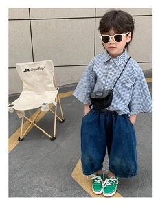 Détails d'un ensemble mode enfant avec chemise à carreaux bleue, jean large et sac noir
