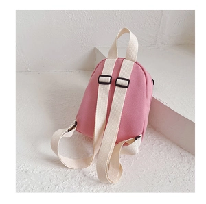 Detail of pink canvas toddler backpack with adjustable white straps on minimalist stand