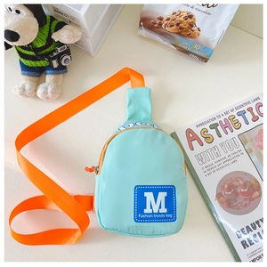 Detail der mintgrünen Nylontasche mit blauem M-Logo-Patch und leuchtend orangefarbenem Gurt
