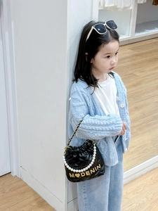 Girl wearing black quilted bucket bag with pearl handle and golden metal lettering detail