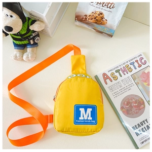 Detailsicht der gelben Kinder-Brusttasche mit orangefarbenem Gurt und M-Logo-Aufnäher