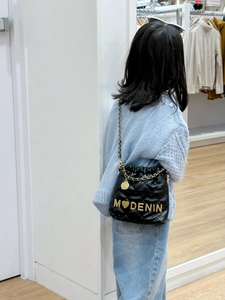 Quilted black bucket bag with gold letter charm and chain strap shown on child model