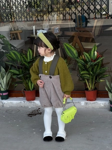 Fillette portant un cardigan vert et une salopette marron avec un sac à main selle