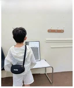 Close-up of a child wearing a black canvas crossbody bag with white GAME lettering detail