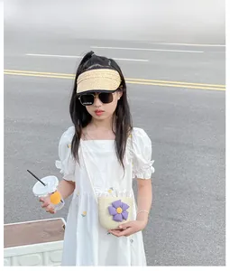 Détail d'enfant portant un sac en paille à fleur mauve et un chapeau de paille visière