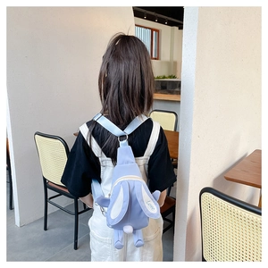Détail d'un sac à dos lapin bleu clair avec broderie Love porté par un enfant au café