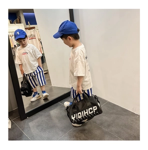 Jeune enfant portant un grand sac de voyage en toile noire avec lettrage blanc en magasin