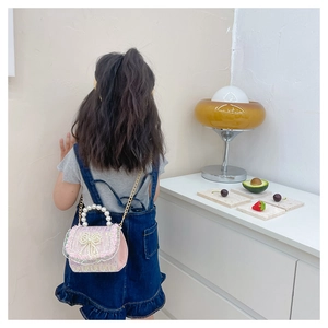 Détail du sac enfant rose à paillettes avec nœud de perles et bandoulière dorée