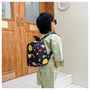 Rear view of a child wearing a lightweight canvas dinosaur backpack with space patterns
