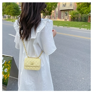 Détail d'un sac bandoulière jaune matelassé avec chaîne dorée et fermoir pivotant