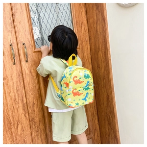 Toddler wearing a small yellow backpack with colorful dinosaur prints outdoors