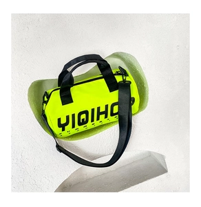 Détail du sac cylindrique vert néon en toile avec sangles noires et lettrage imprimé
