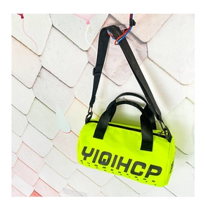 Sac de voyage cylindre vert fluo avec imprimé lettres accroché sur un mur carrelé