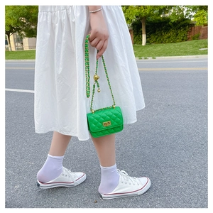 Détail d'un mini sac bandoulière matelassé vert avec chaîne dorée sur robe blanche