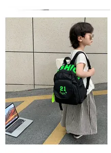 Side view of black nylon kids backpack with neon green lettering on a child outdoors