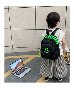 Rear view of kid's black canvas backpack with neon green fashion text on light tile wall