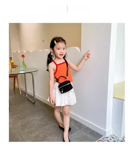 Détail d'un mini sac à main noir en strass assorti à un haut orange et une jupe plissée