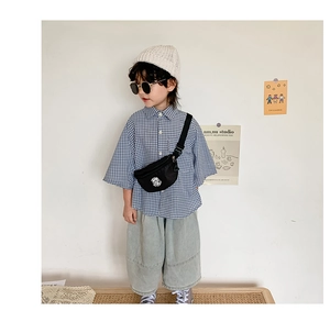 Detail of child wearing a black printed waist bag with blue checkered shirt and grey trousers