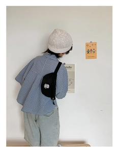Boy's black canvas chest bag with white logo worn over a blue plaid shirt
